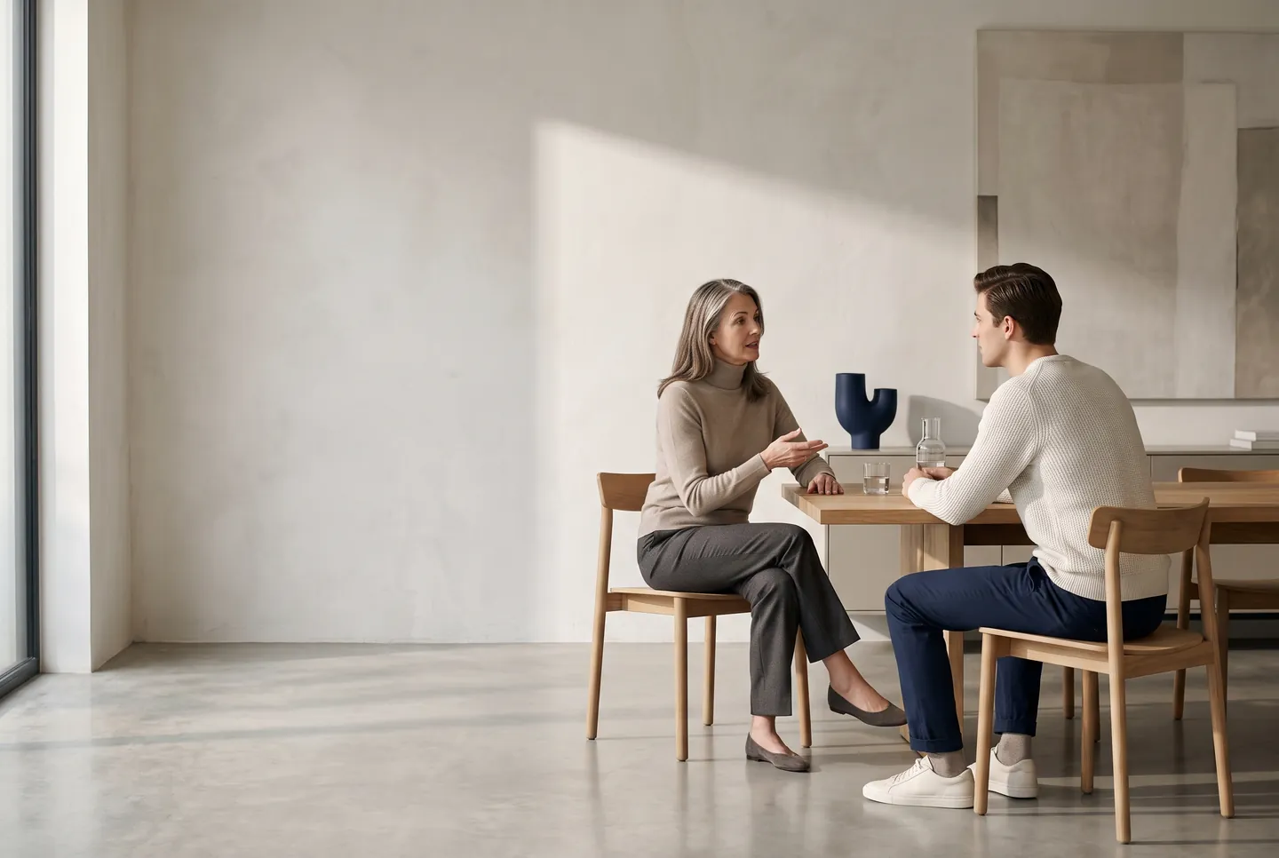 Duas pessoas conversando de frente uma para a outra, à mesa de uma sala clara
